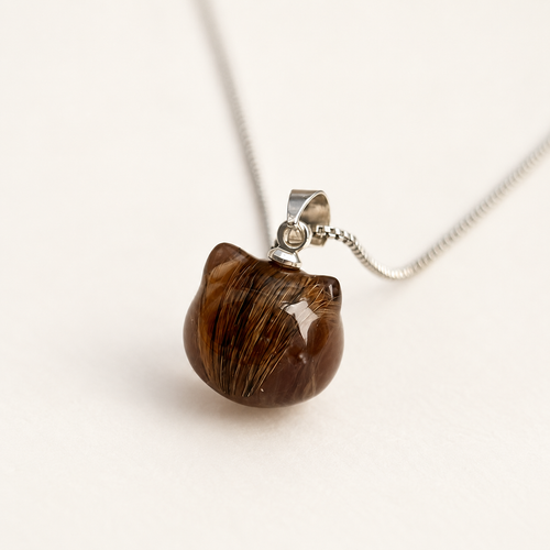 Cat-head-shaped transparent brown resin pendant containing pet fur, with silver-colored top hardware and a fine chain on a light background.
